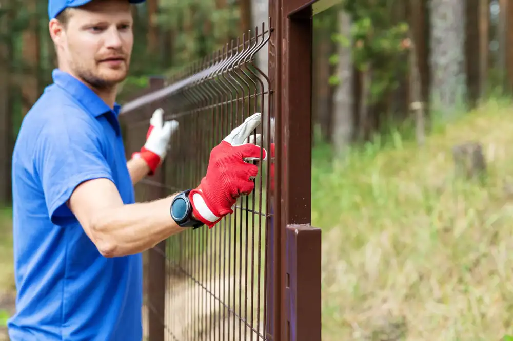 Installer fitting a metal fence panel between posts